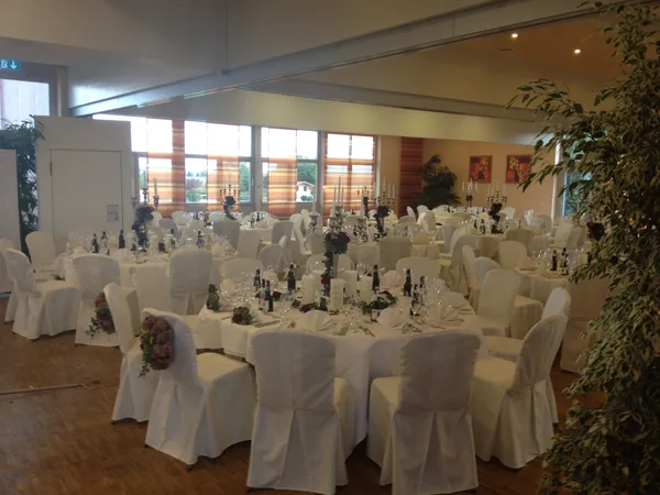 Runde Tische mit weißen Stuhlhussen und Kerzenleuchtern im Saal des Hotel Aramis