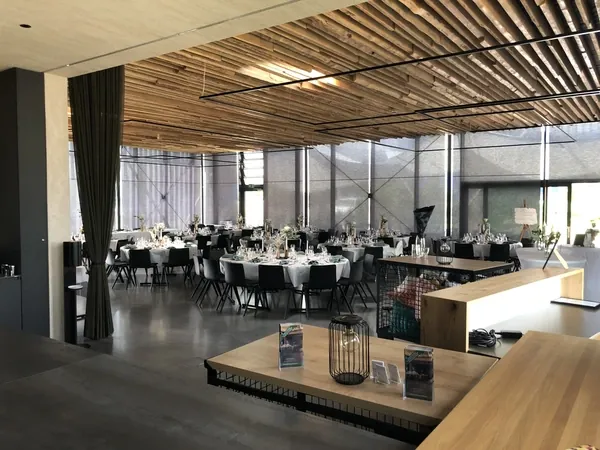 Saal mit offener Holzdecke und runden Tischen in der Event Schneiderei