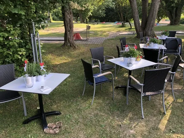 Gartentische mit Blumendeko unter alten Bäumen beim Kovas Balkan Restaurant