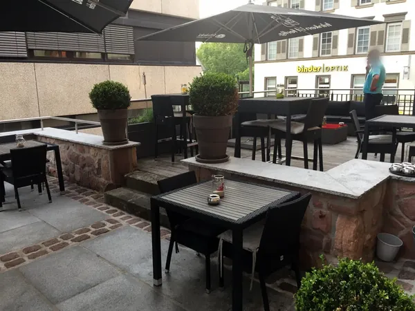 Terrasse mit Tischen und Sonnenschirmen am Mauerwerk