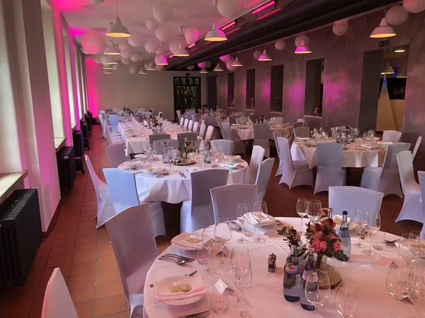 Lange Tafeln und runde Tische mit rosa Ambientelicht im Saal des Quartier77