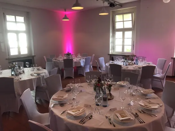 Gedeckte runde Tische unter Industrieleuchten mit rosa Licht im Quartier77