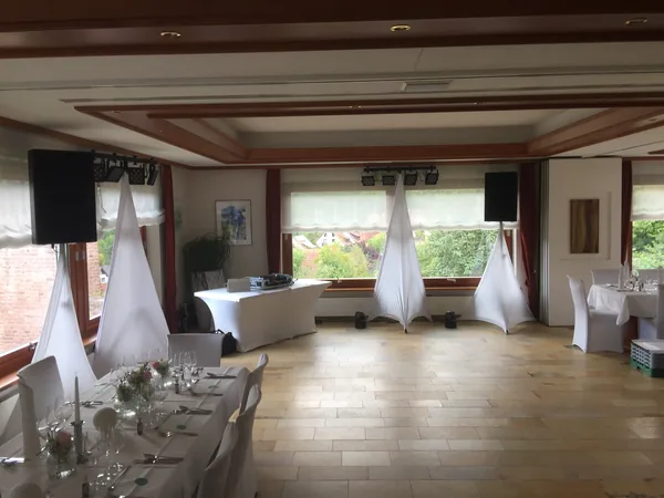 Saal mit DJ-Technik, Lautsprechern und gedeckten Tischen im Restaurant Talblick